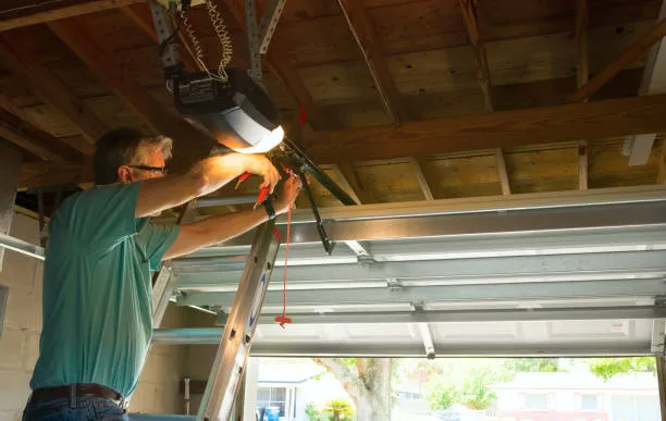 A repair technician on a ladder servicing a residential garage door opener and spring